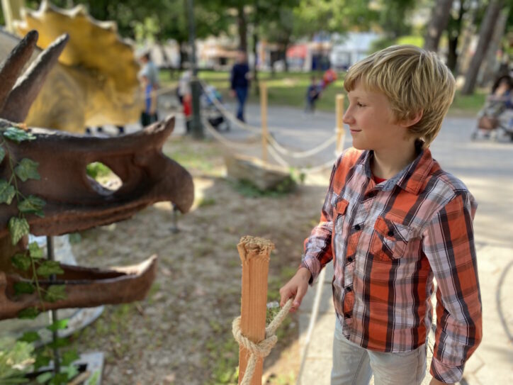 Little boy in the park with exhibition of dinosaurs, nose summer day